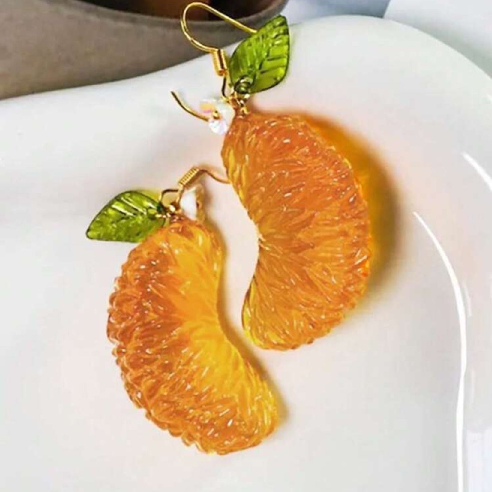 Orange slice earrings with green leaves on a white plate
