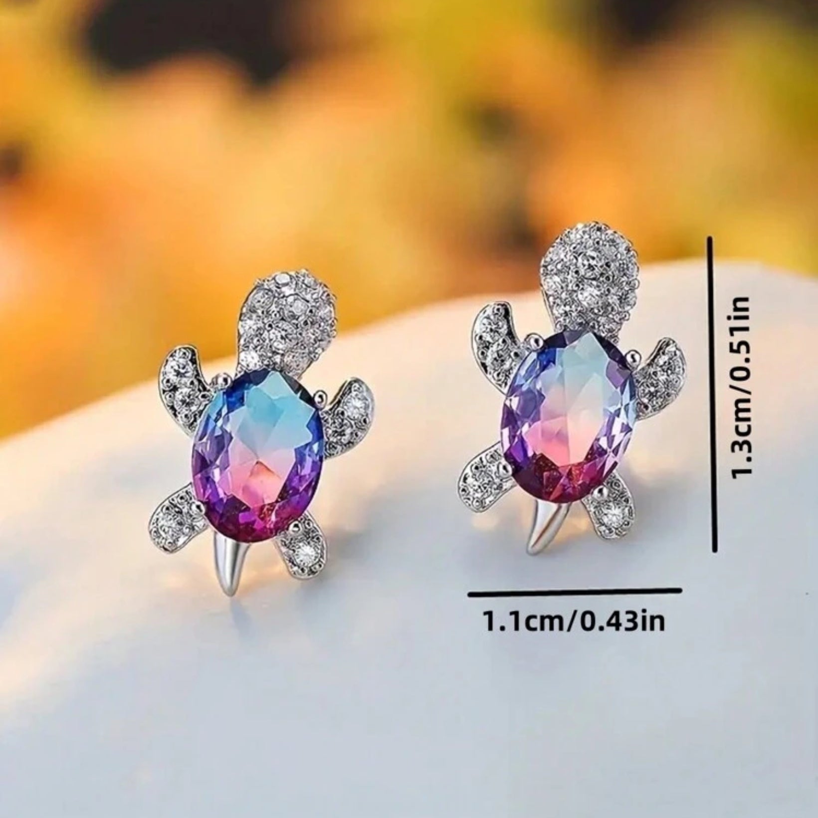 Turtle-shaped earrings with colorful gemstones and measurements on a blurred background