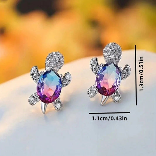 Turtle-shaped earrings with colorful gemstones and measurements on a blurred background