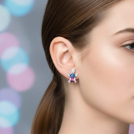 Close-up of a woman wearing a Multicolor Crystal Turtle Earring with a blurred multicolored background