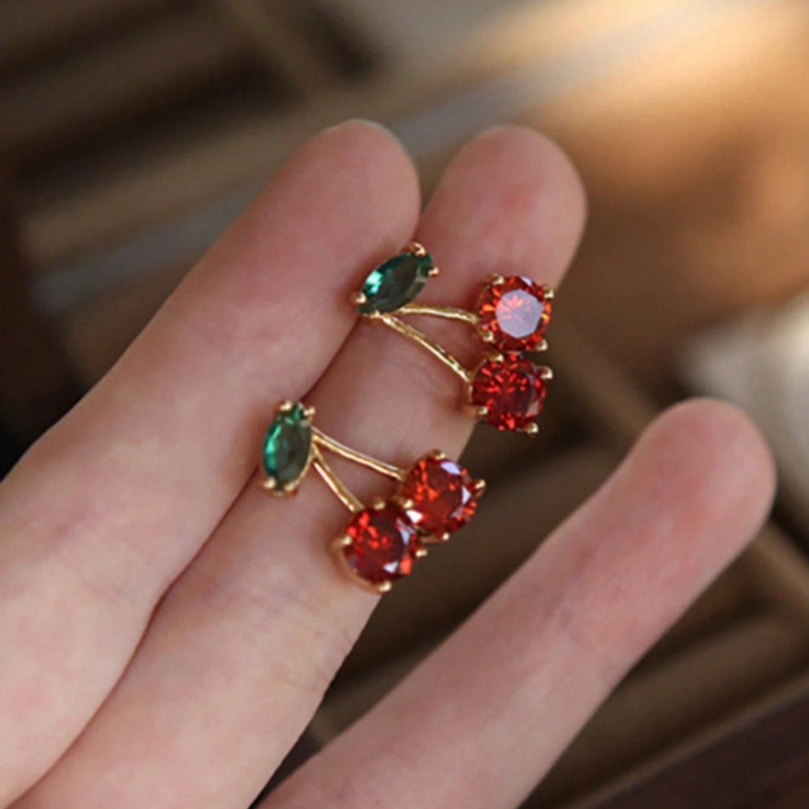 Gold ring with red and green gemstones on a hand against a blurred background