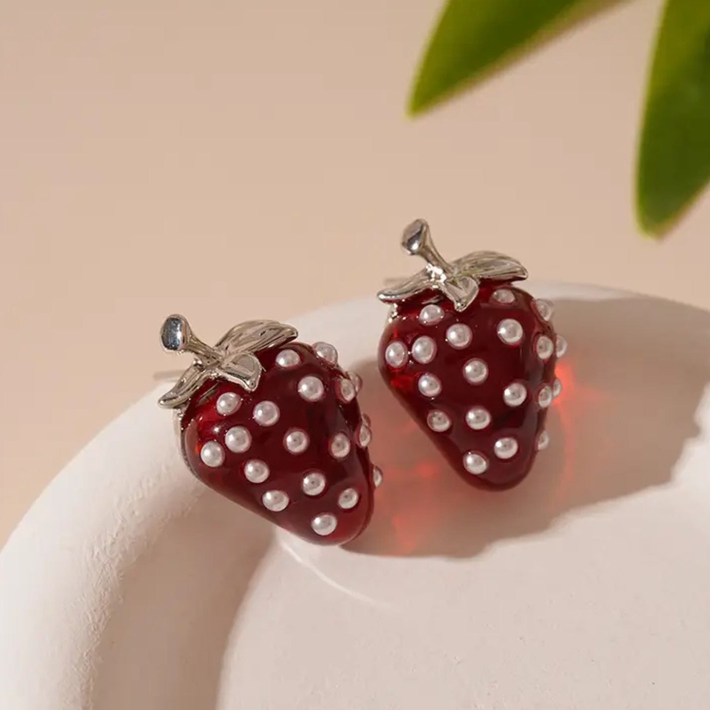 Strawberry-shaped earrings with pearl details on a beige background
