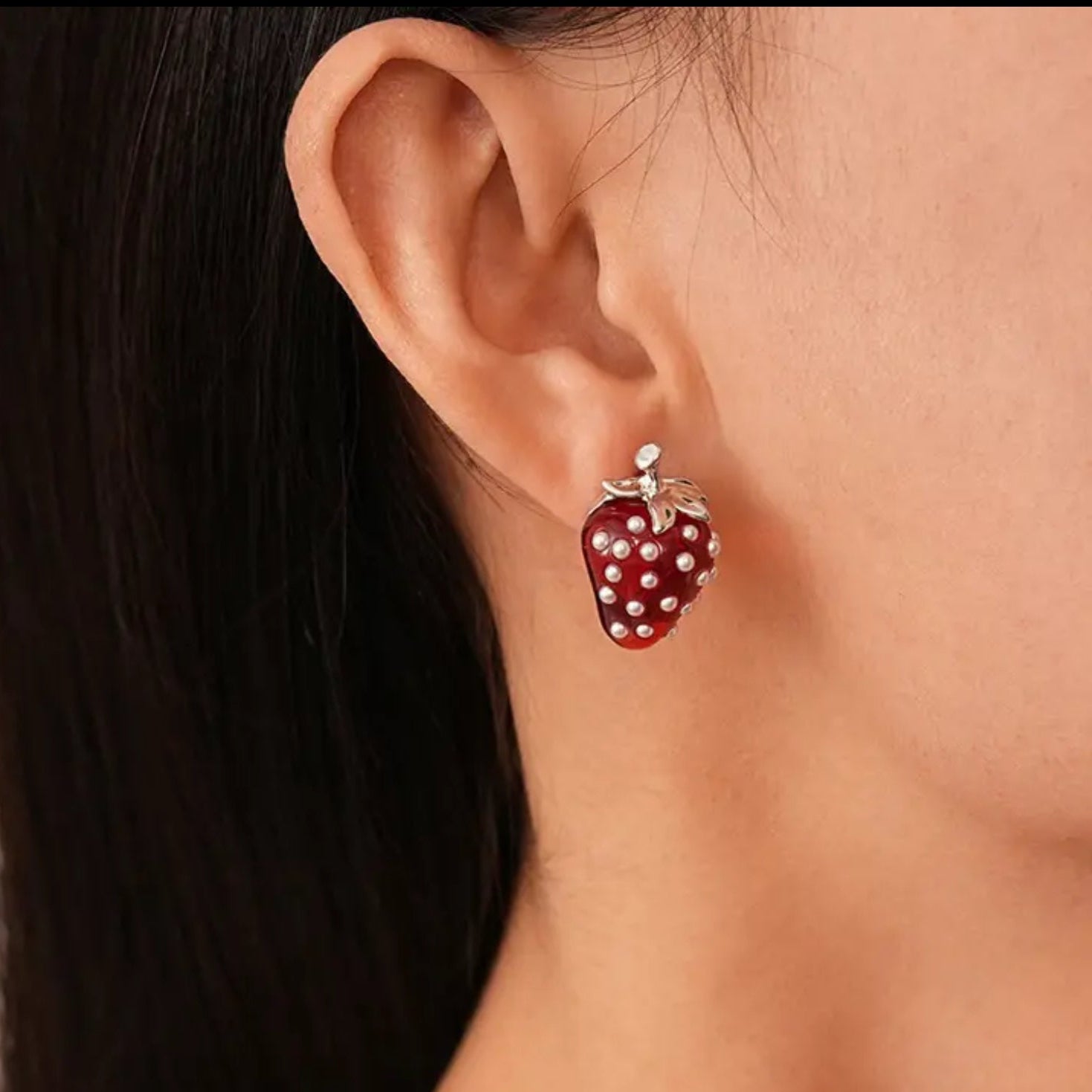 Close-up of a strawberry-shaped earring worn on an ear.