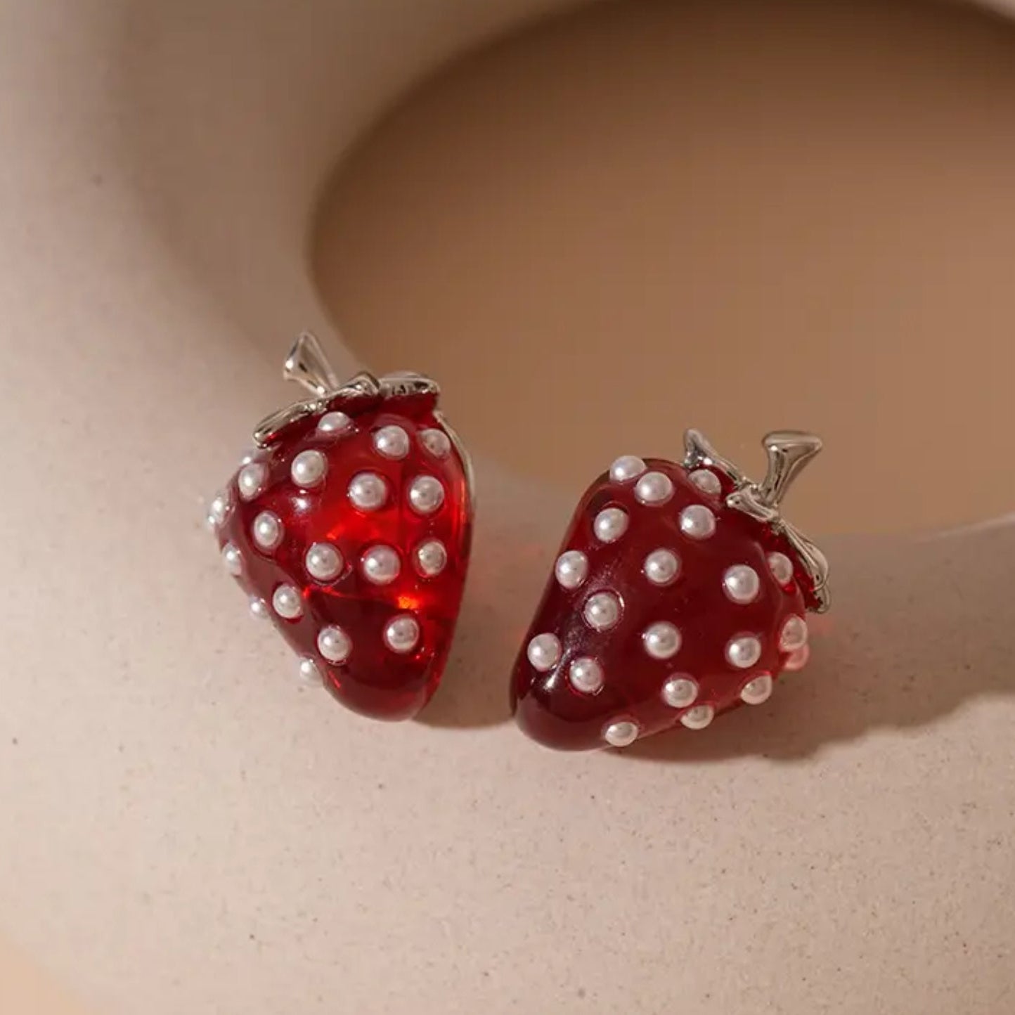 Strawberry-shaped earrings with pearl details on a beige background