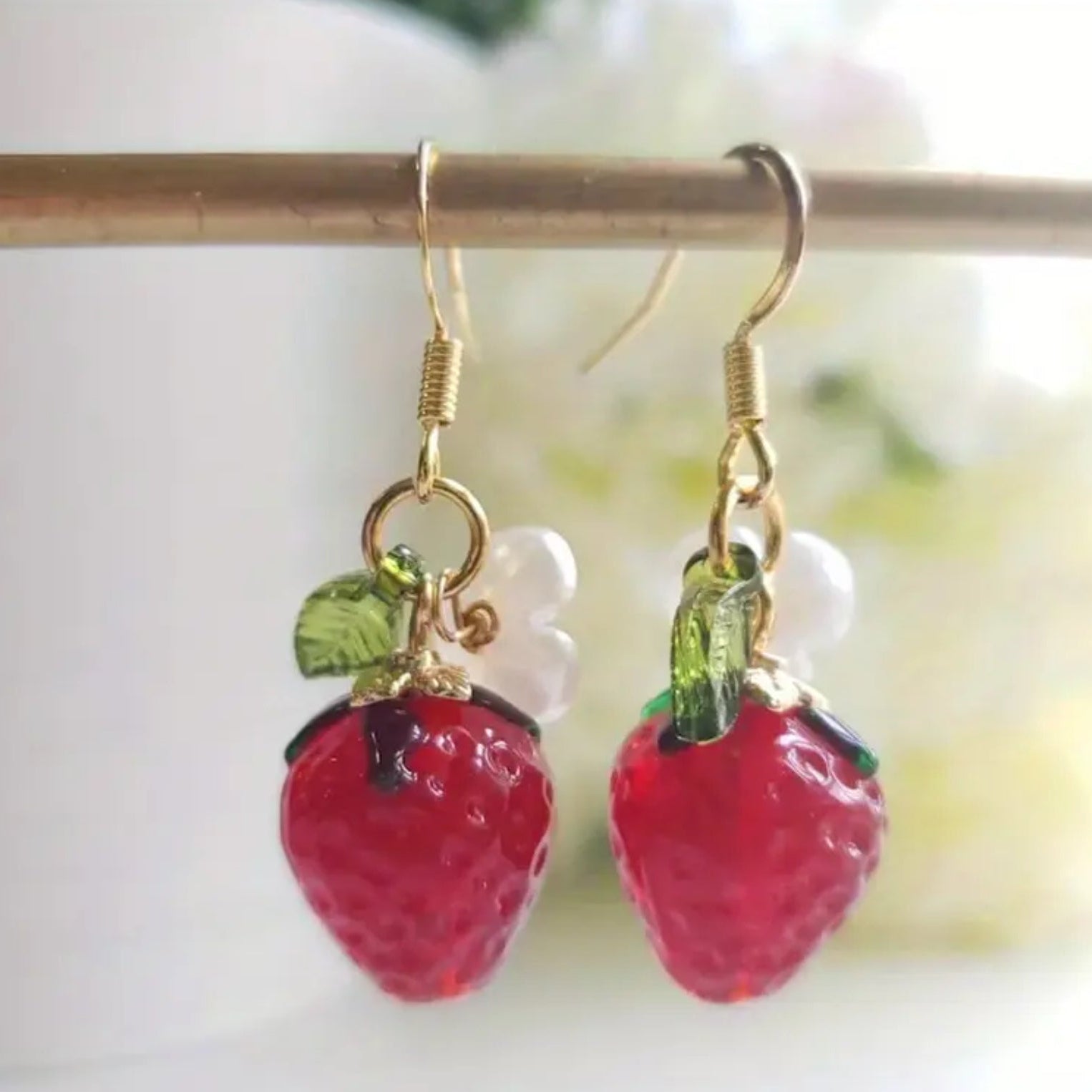 Strawberry-shaped earrings with gold hooks on a white background