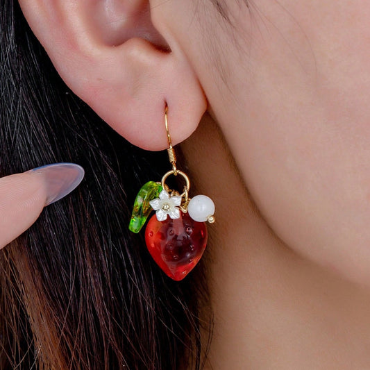 Close-up of a person wearing a decorative earring with a red strawberry and pearl design.