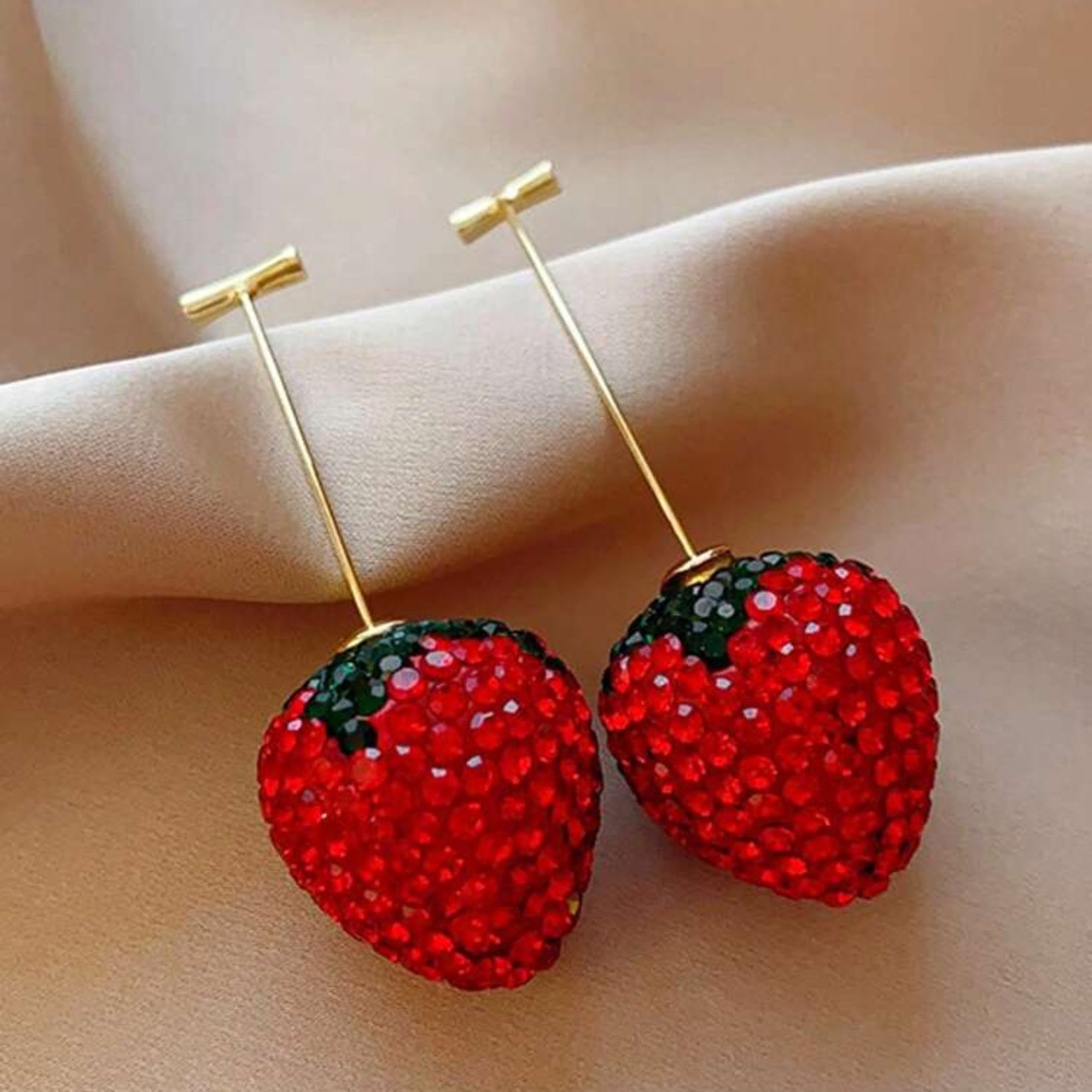 Red strawberry-shaped earrings on a beige surface