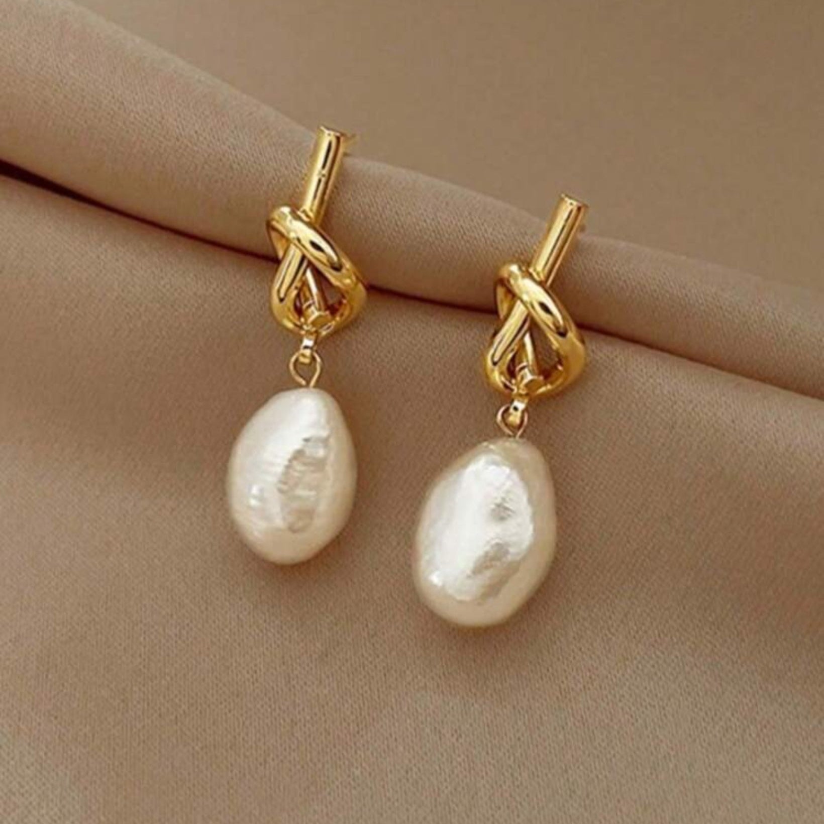 Gold earrings with pearl drops on a beige surface
