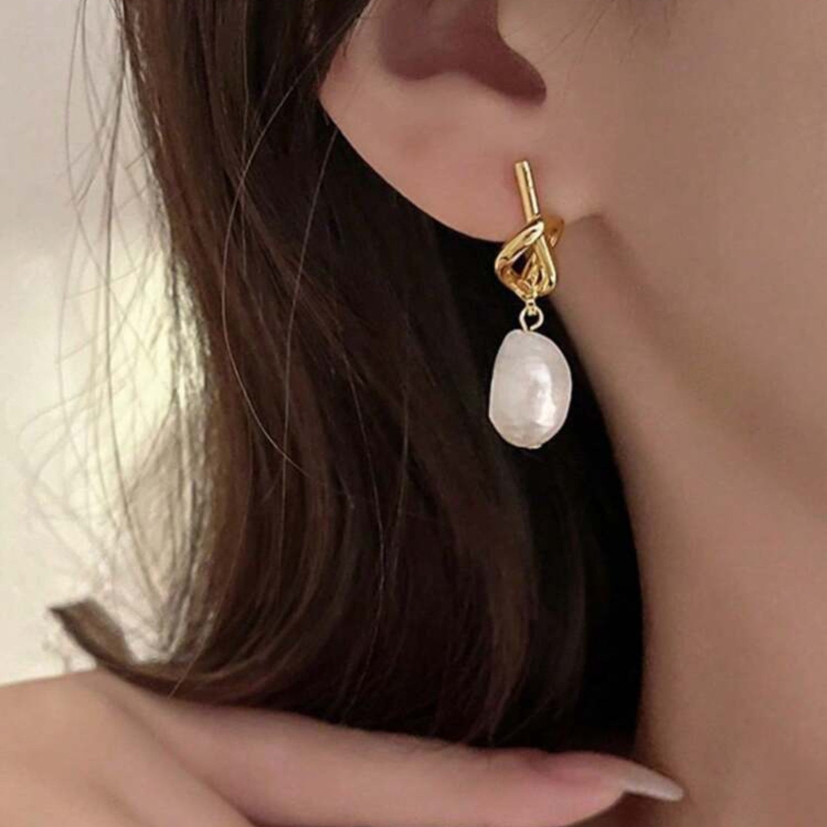 Gold earring with a pearl drop worn by a person