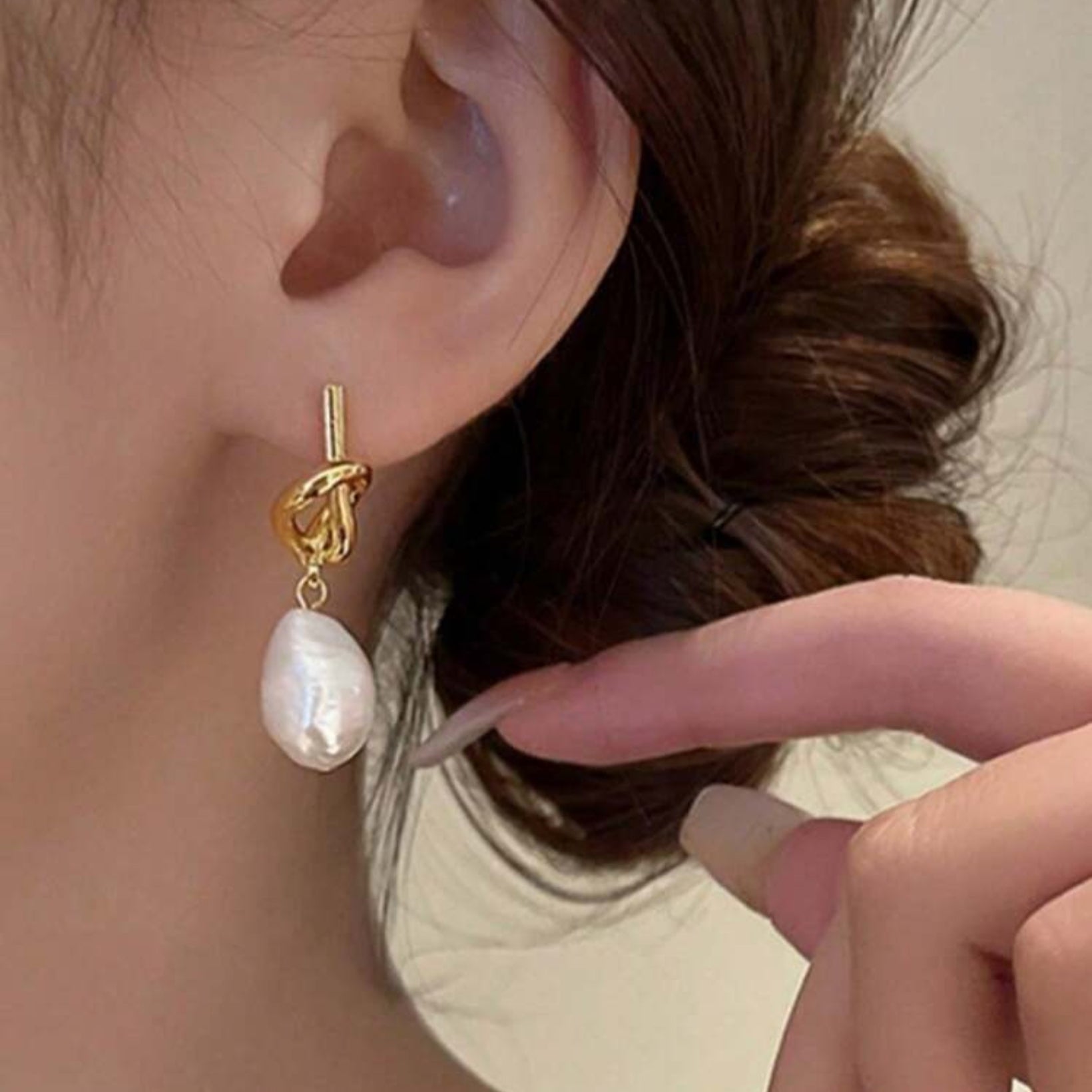 Gold knot earring with a pearl drop worn by a person.