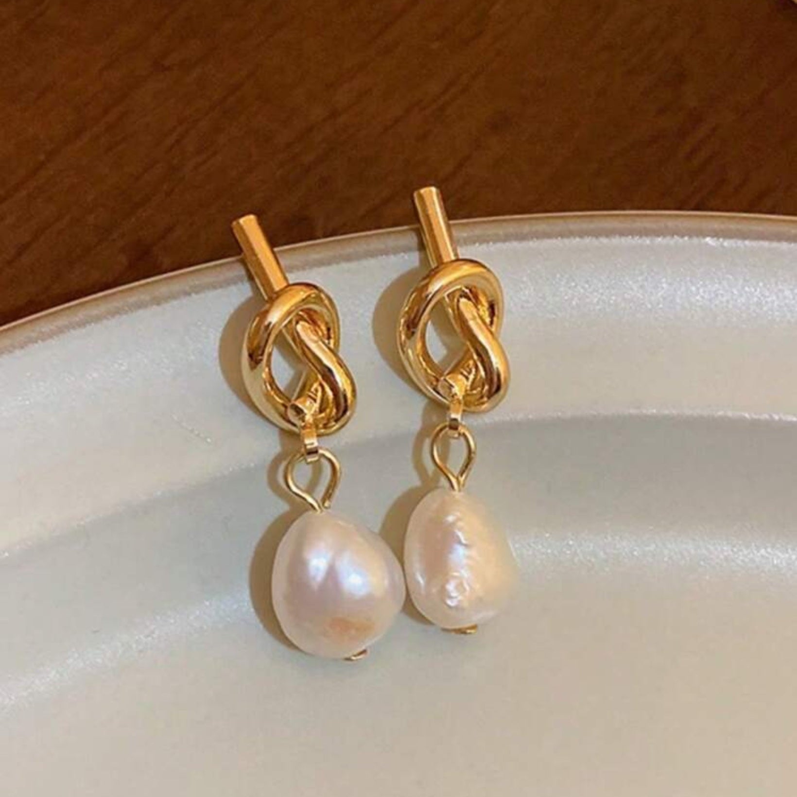 Gold earrings with pearl drops on a white plate