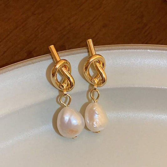 Gold earrings with pearl drops on a white plate