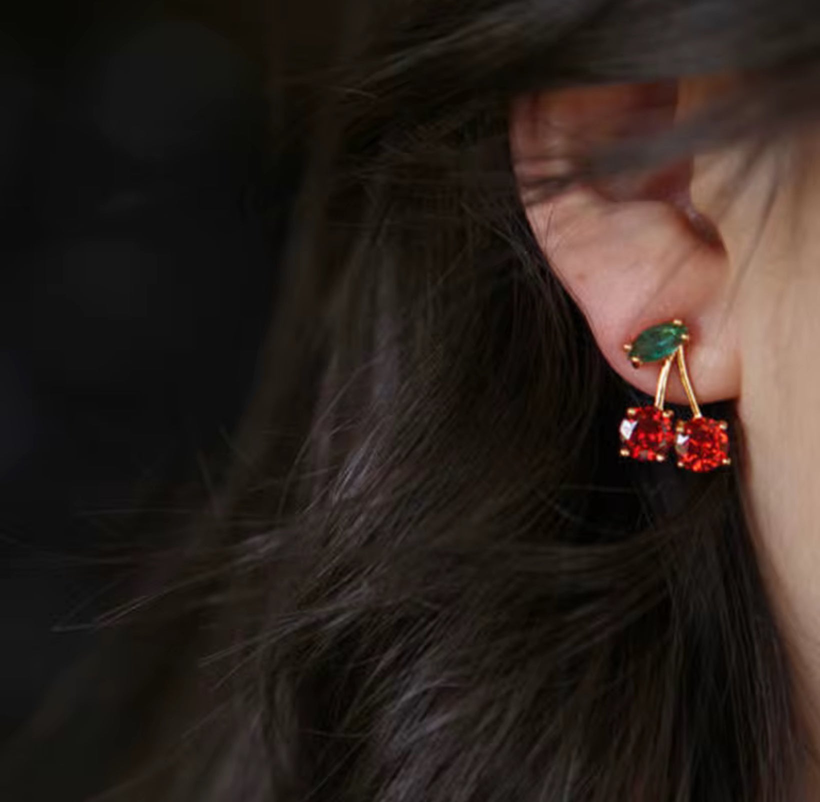 Close-up of a person wearing red and green gemstone earrings with dark hair.