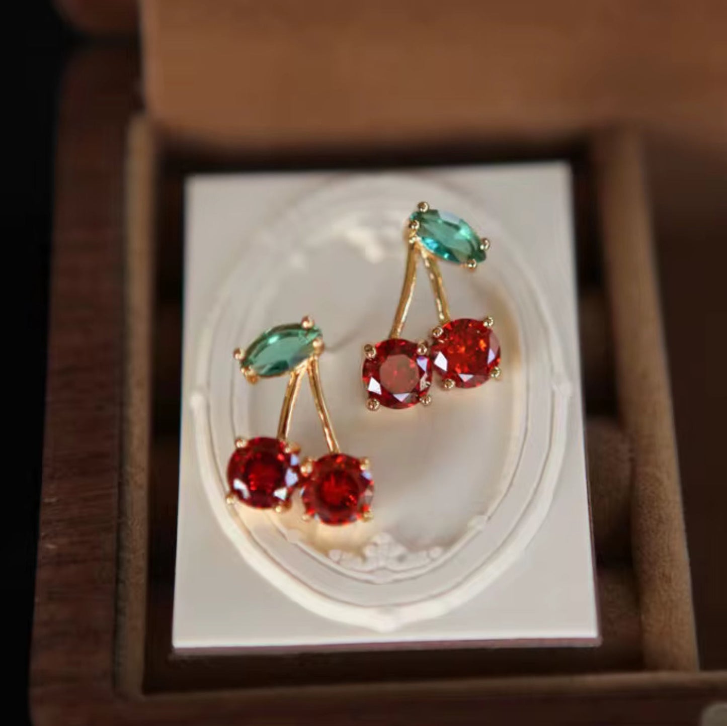 Cherry-themed earrings with red and green gemstones in a box