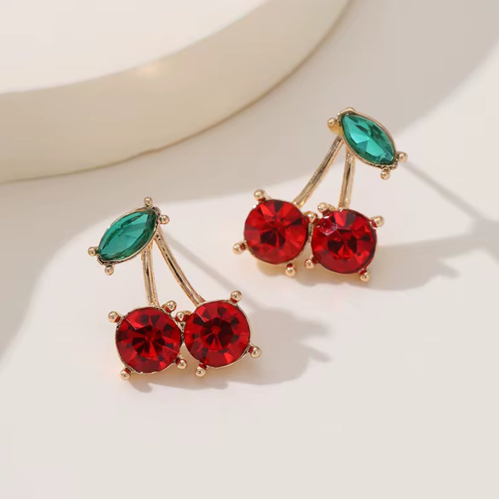 Gold cherry-shaped stud earrings with red gem stones and green enamel leaf accents