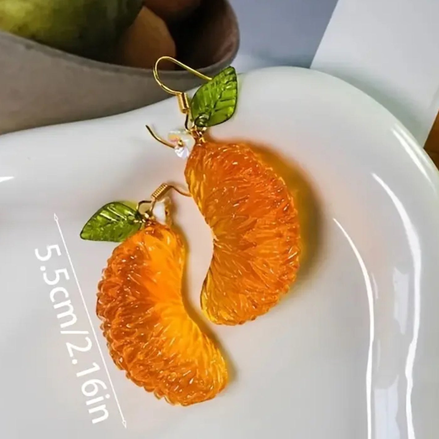 Orange slice earrings with green leaves on a white plate