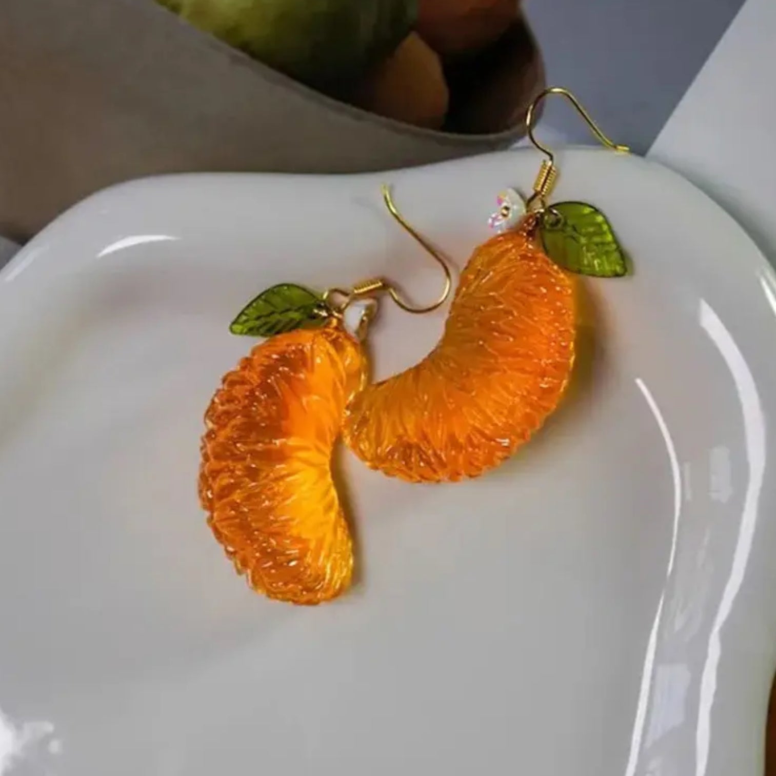 Orange-shaped earrings with green leaves on a white dish