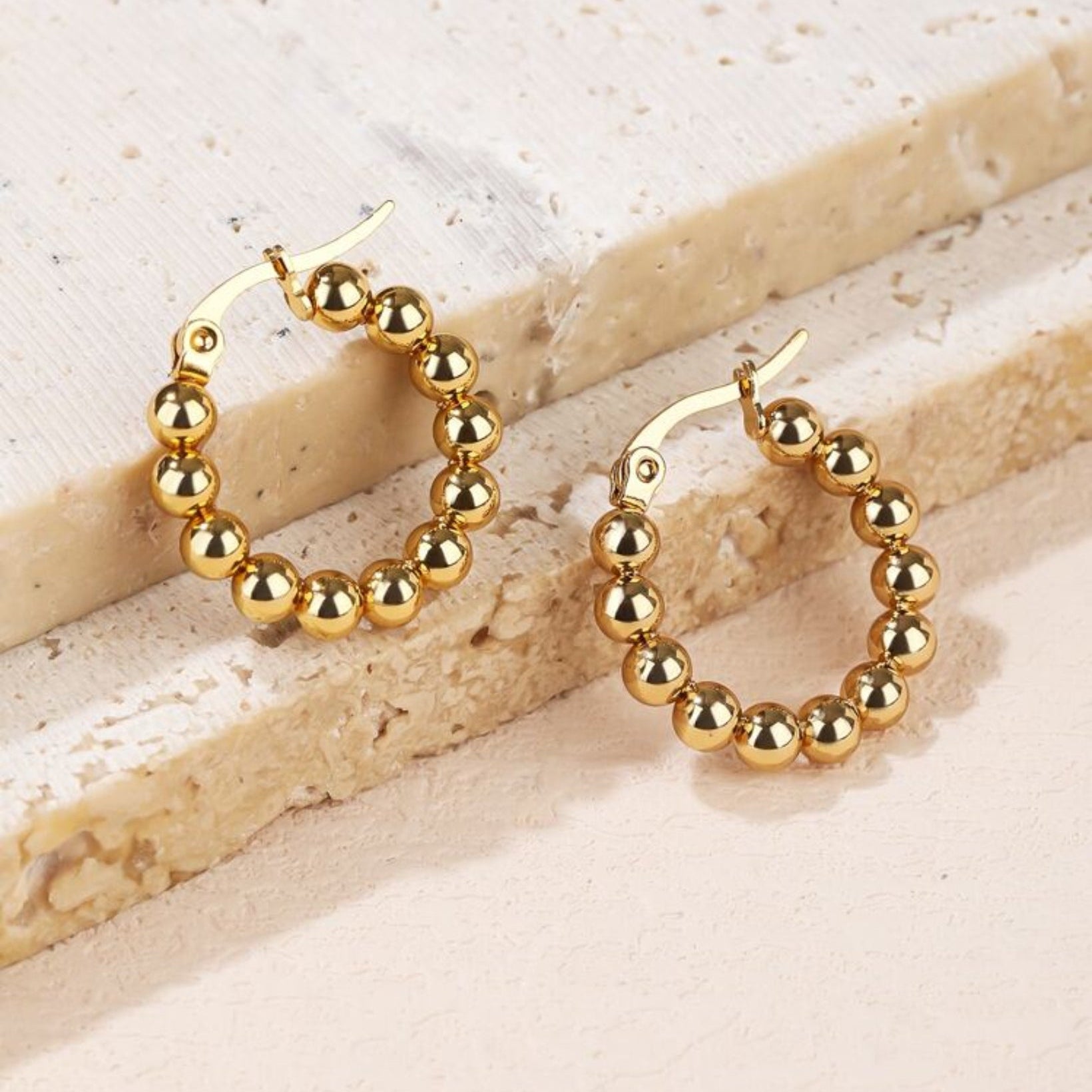 Gold hoop earrings with bead detailing on a light stone background