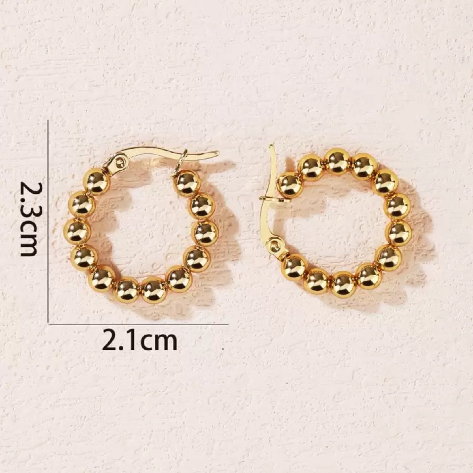 Gold hoop earrings with measurements on a light pink background