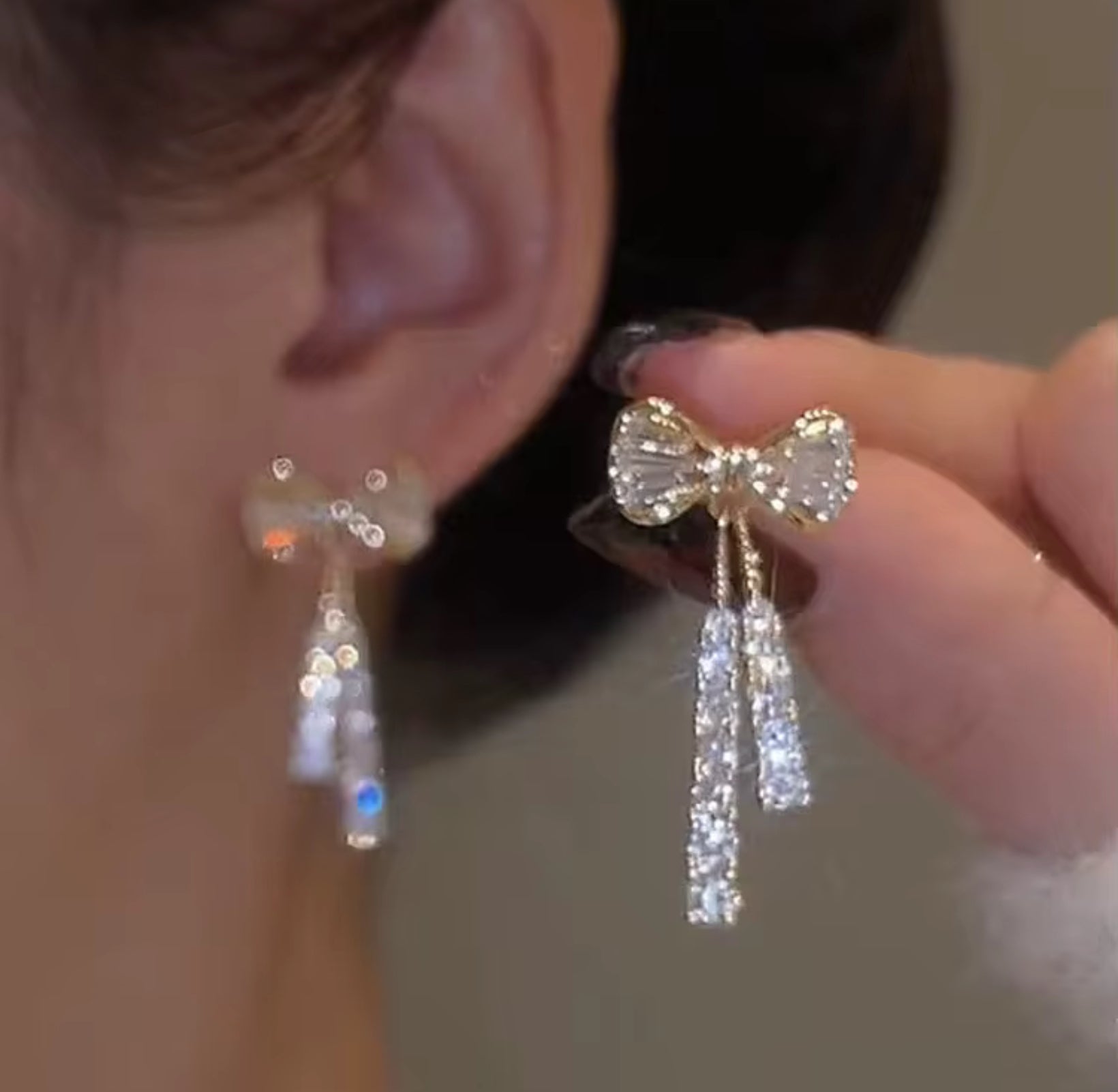 Close-up of a person wearing bow-shaped earrings with dangling crystals.
