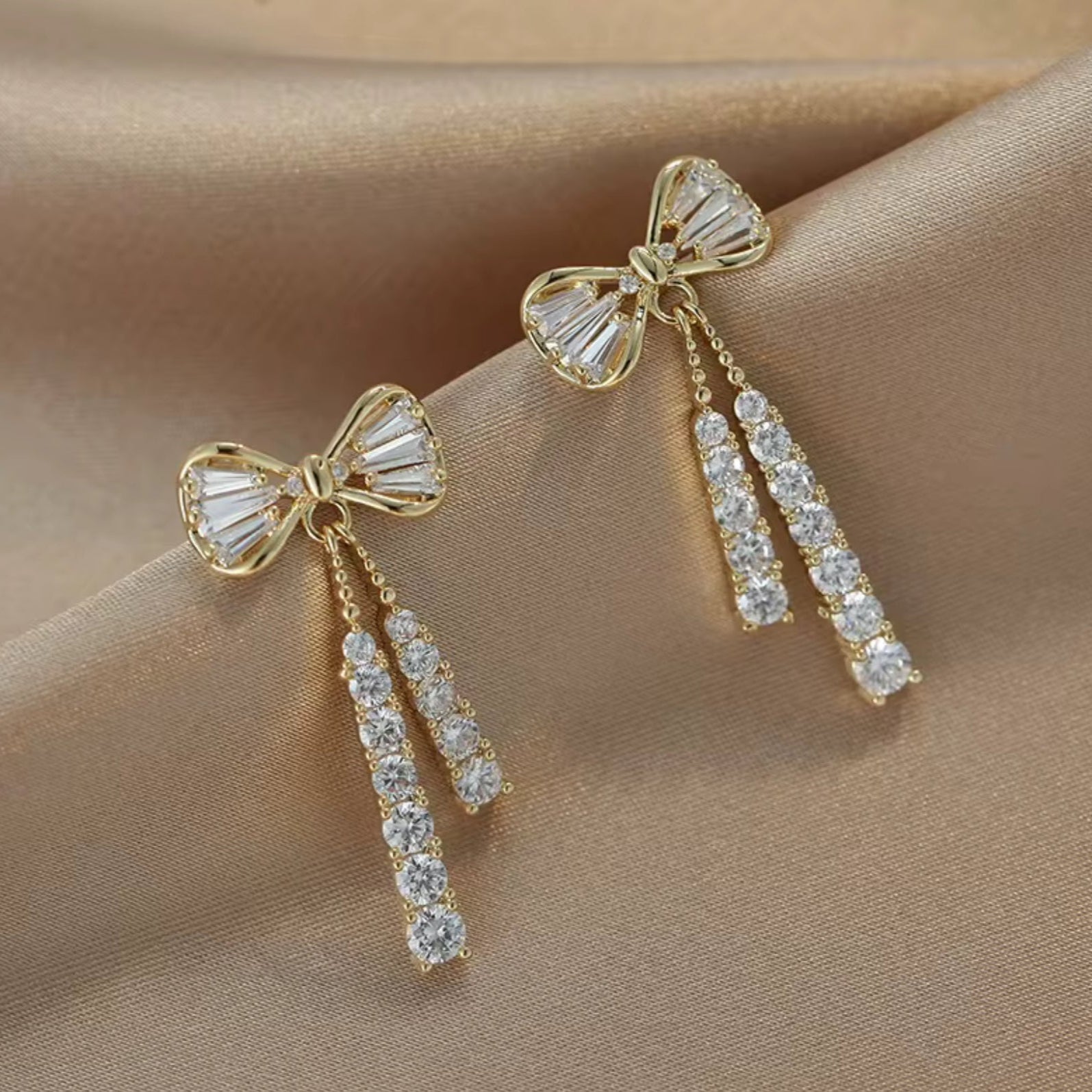 Gold bow-shaped earrings with diamond accents on a beige fabric background
