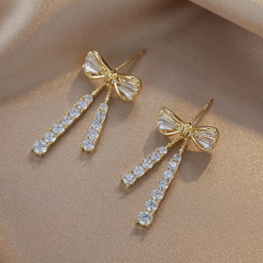 Gold bow earrings with clear gemstones on a beige background