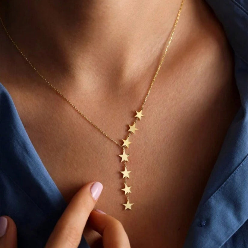 Gold star necklace on a person's neck with a hand pointing to it, wearing a blue top.