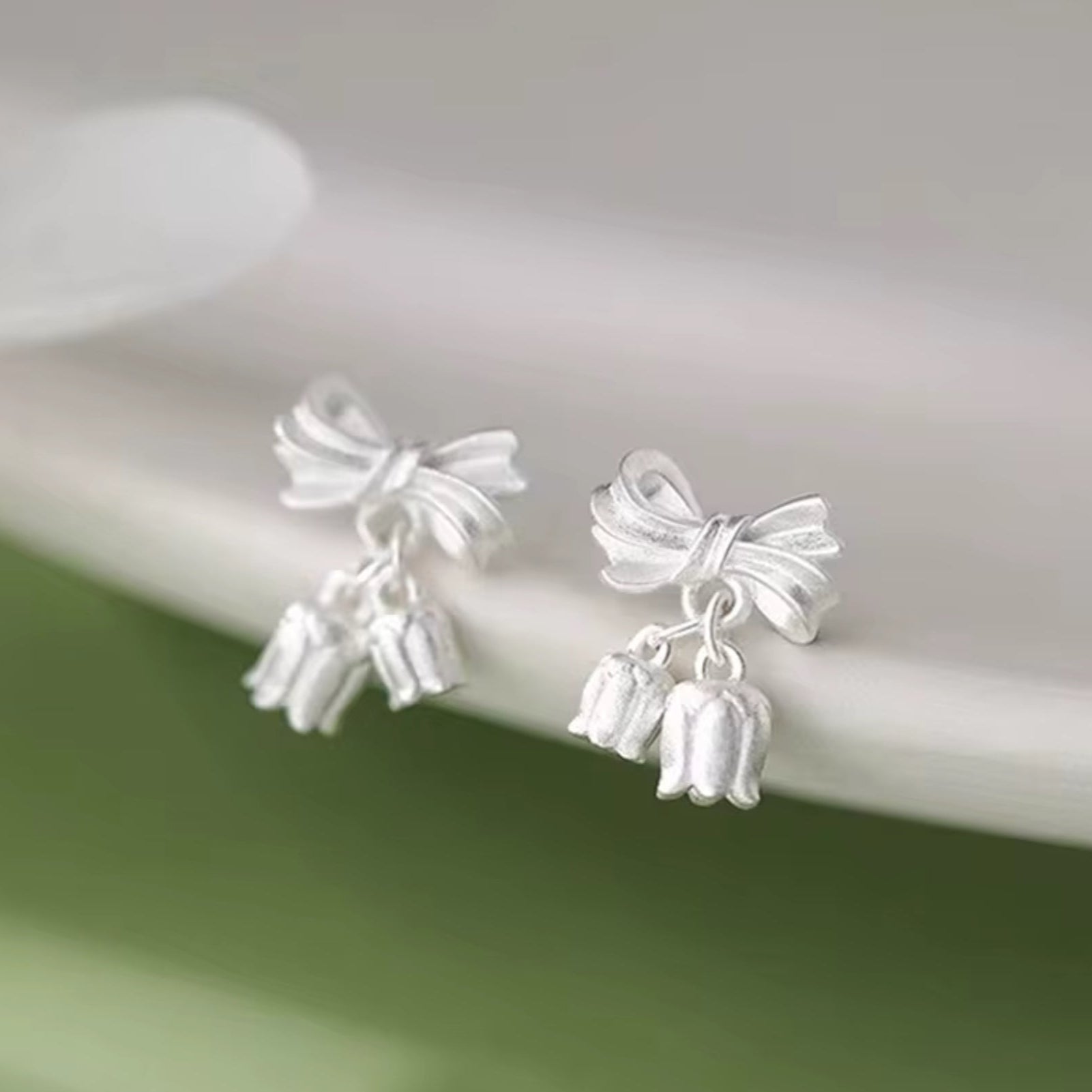 Silver bow-shaped earrings with dangling elements on a white surface.