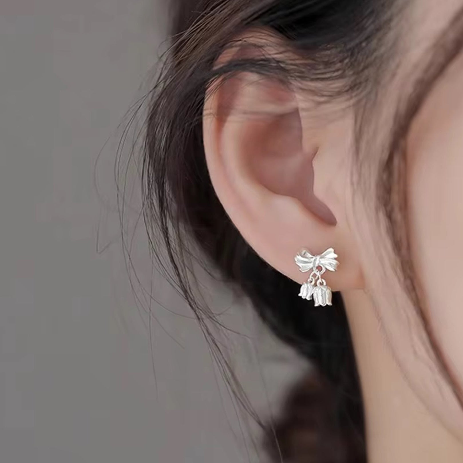 Silver bow-shaped earrings worn by a person with a neutral background