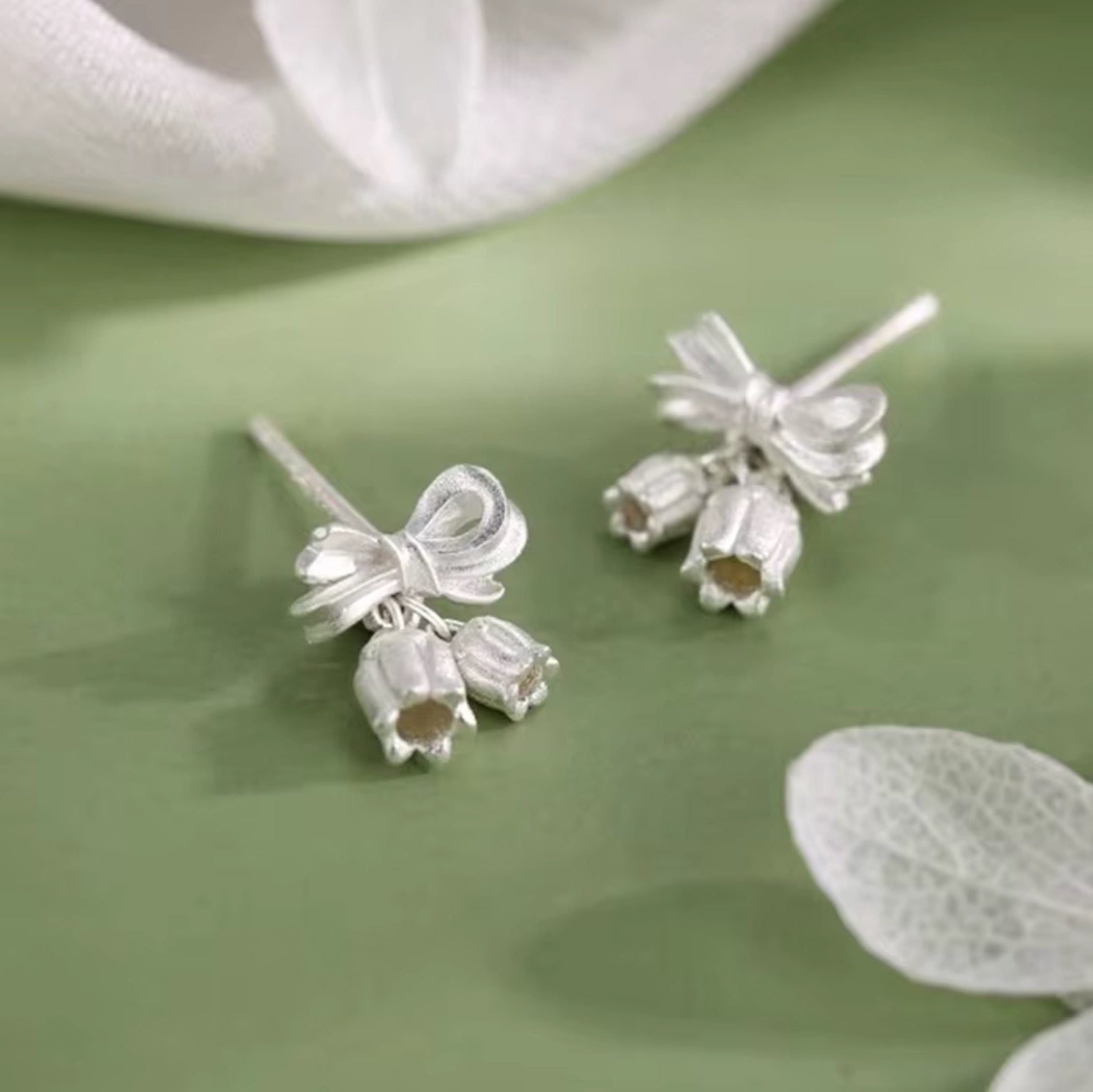 Silver earrings with bow and flower designs on a green surface