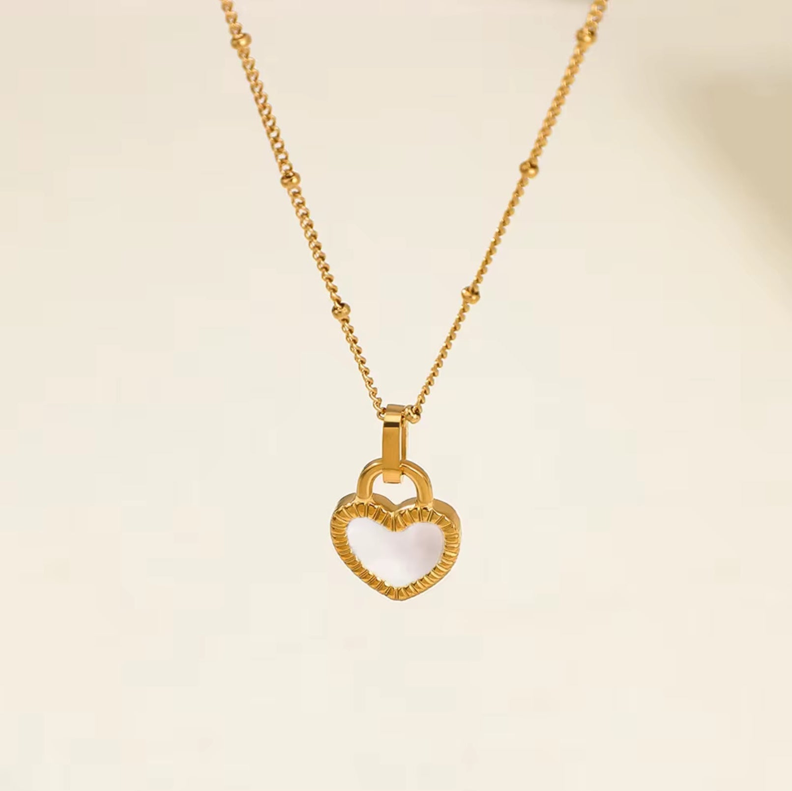 Gold necklace with a heart-shaped pendant on a beige background