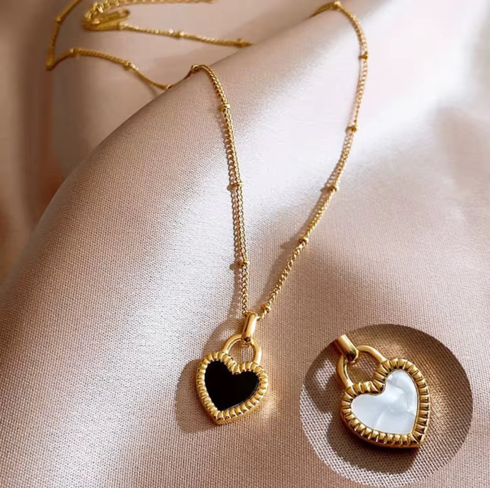Gold necklaces with black and white sides, heart-shaped pendants on a beige fabric background