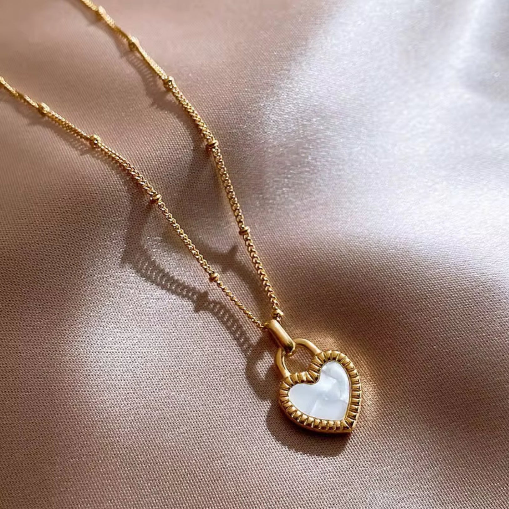 Gold necklace with a heart-shaped pendant on a beige fabric background
