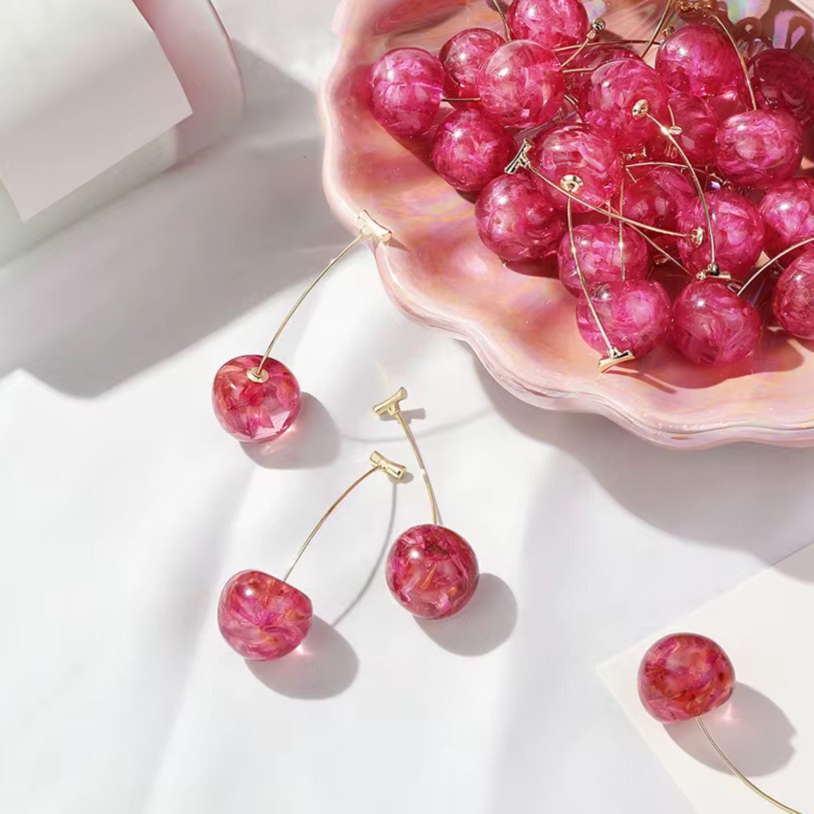 Pink cherry-themed earrings on a white surface with a pink shell and cherry stones.