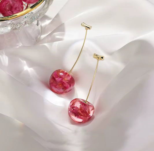 Pink cherry-shaped earrings on a white fabric background