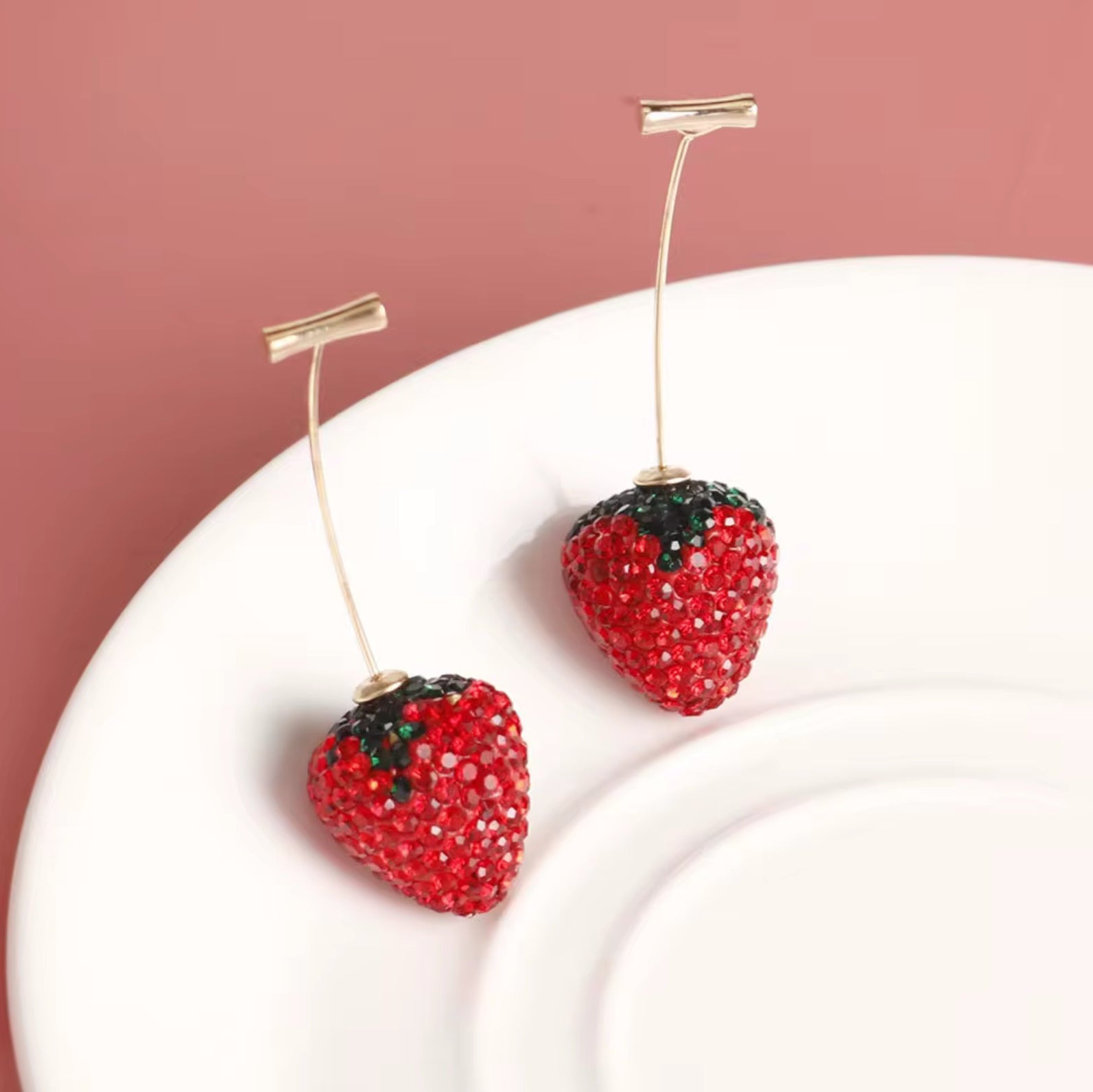 Strawberry-shaped earrings on a white plate with a pink background