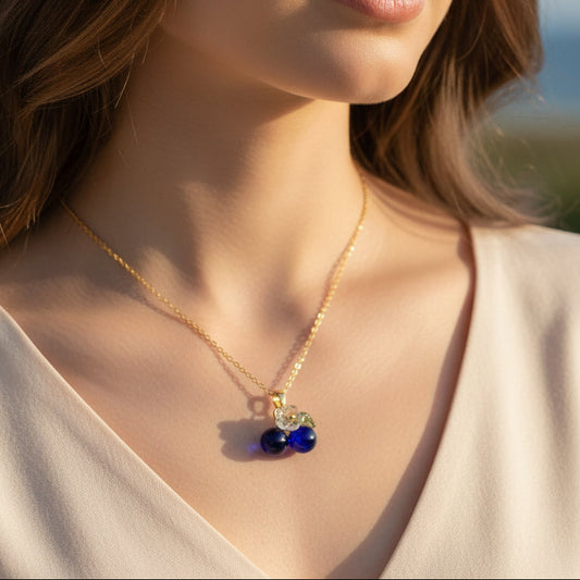 Necklace with blue beads and a leaf charm on a white surface with a plant in the background
