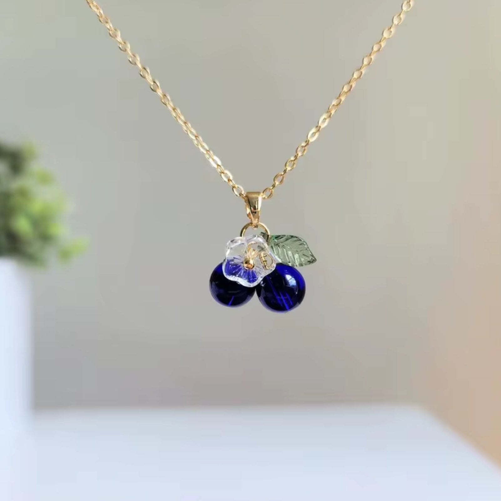Gold necklace with blue berry pendants on a neutral background
