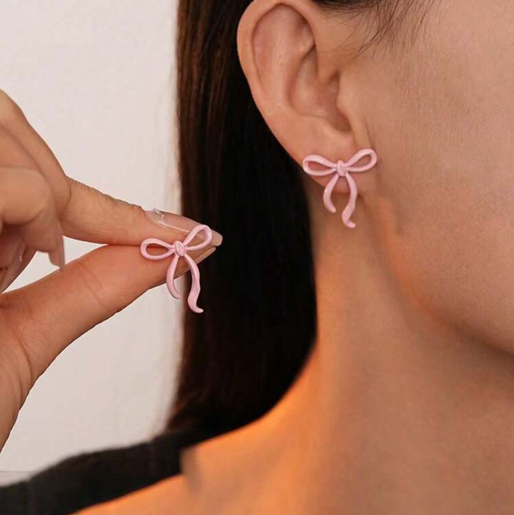 Person wearing pink bow-shaped earrings with one being held in hand against a neutral background