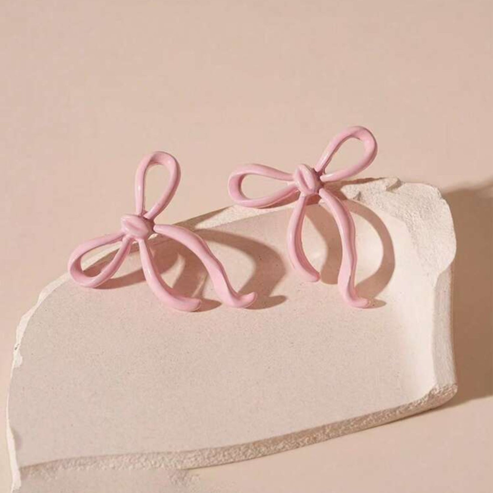 Pink bow-shaped earrings on a textured beige surface with a soft pink background