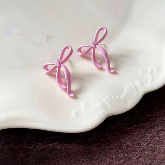 Pink bow-shaped earrings on a white shell