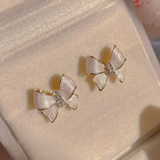 Bow-shaped earrings on a soft pink surface