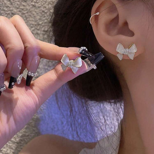 Person wearing a bow-shaped earring with another one held by a hand.