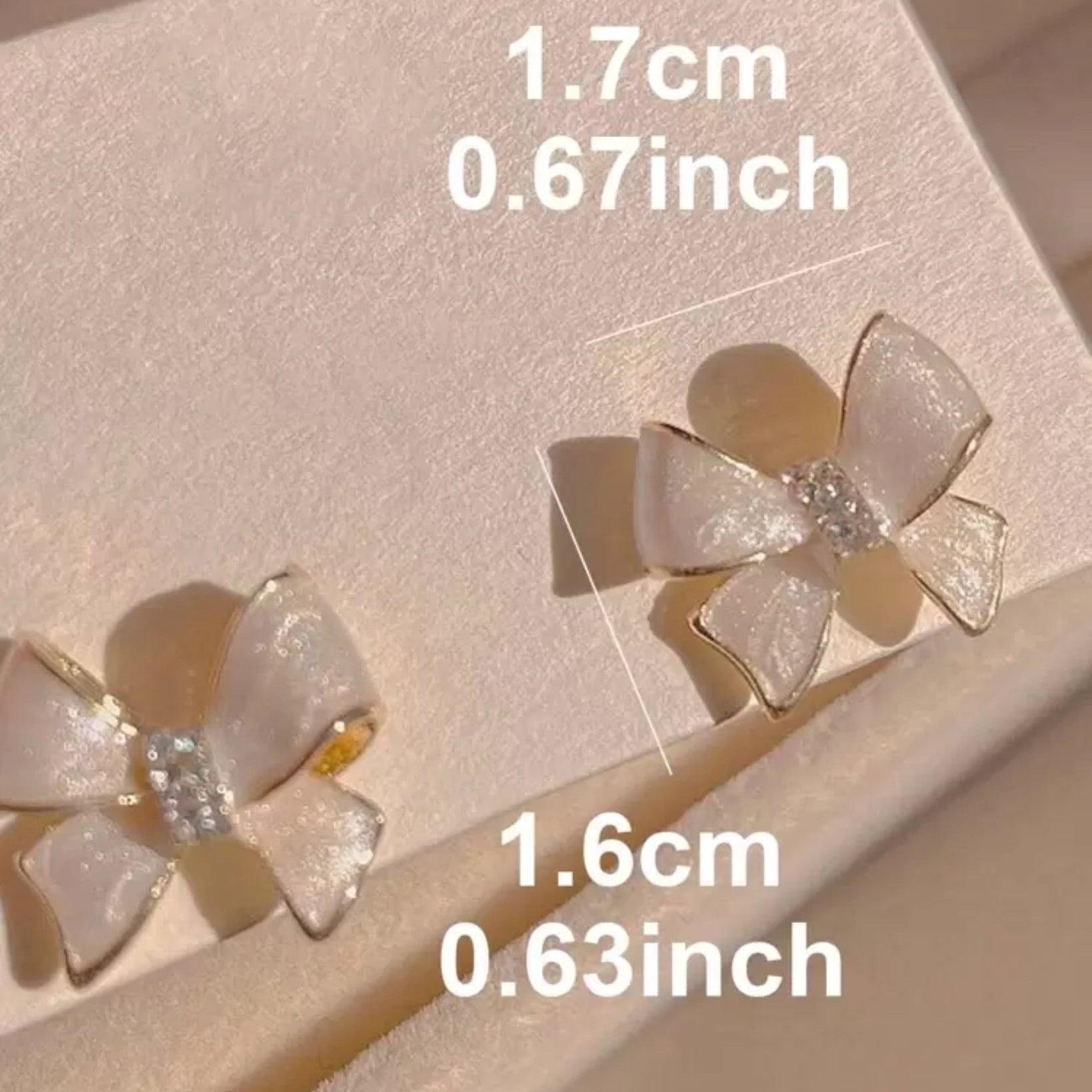 Bow-shaped earrings on a light pink background with measurements displayed.