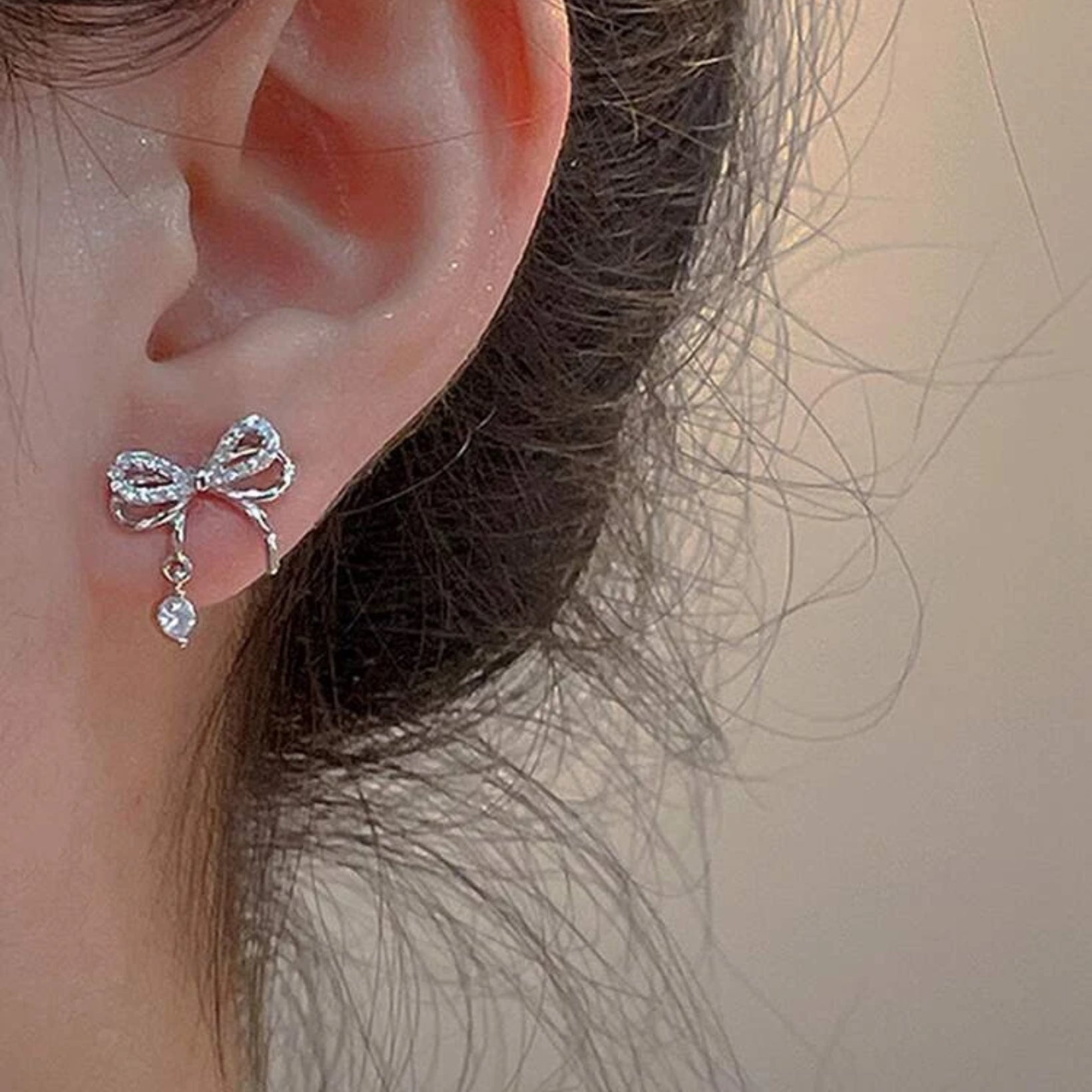 Silver bow-shaped earring worn on an ear with a neutral background