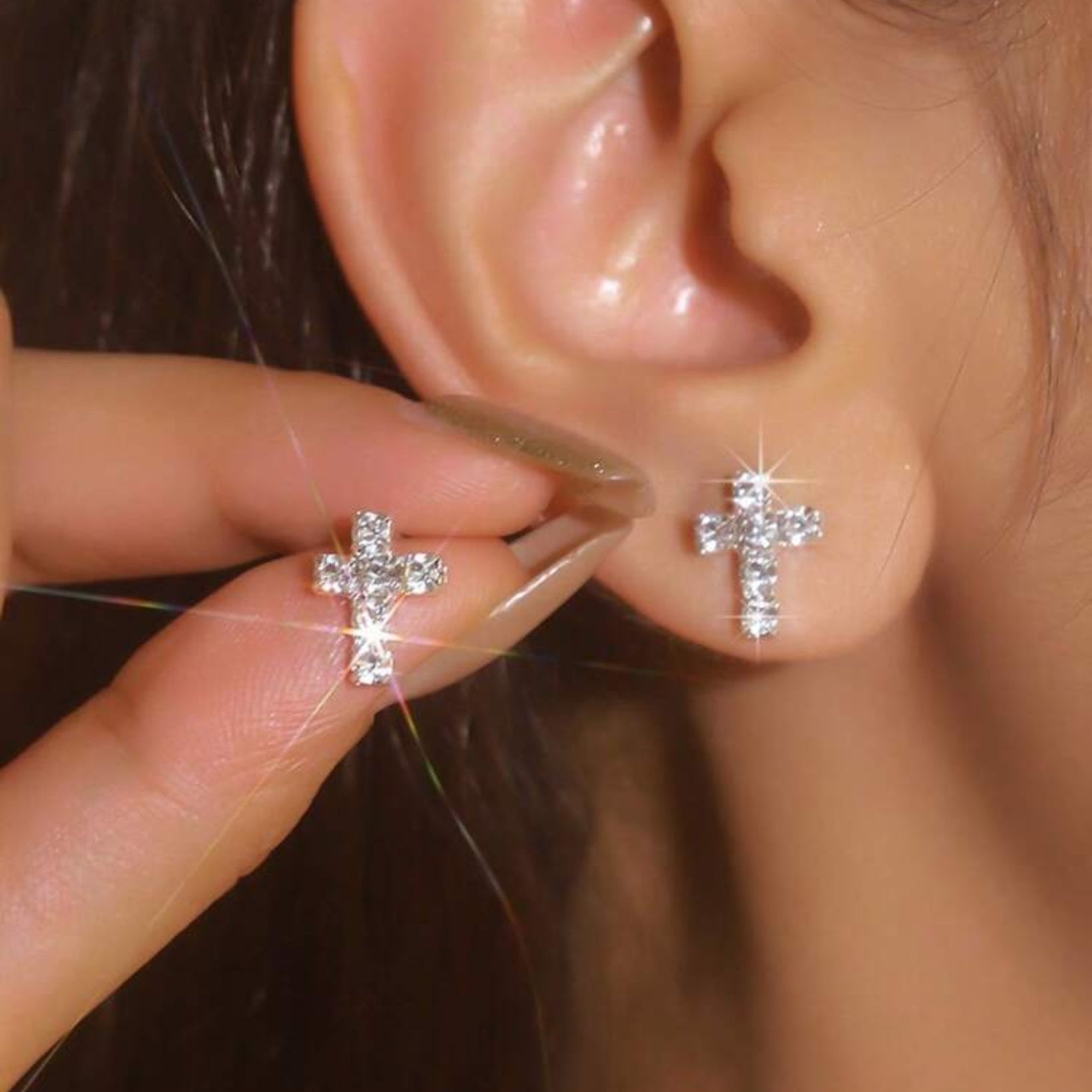 Close-up of a person wearing a silver cross earring with another one held in hand.