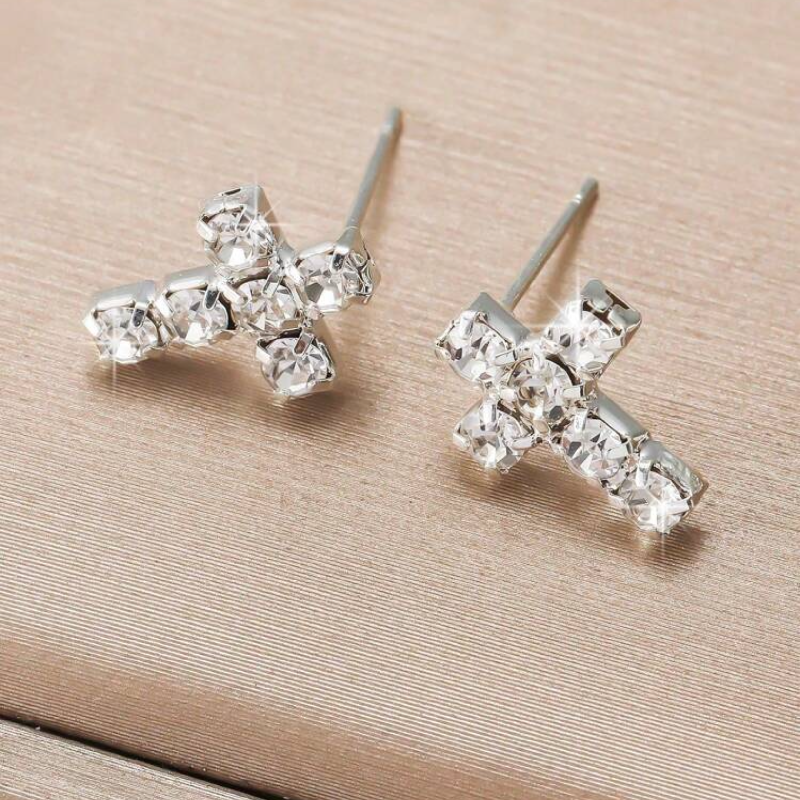 Silver cross-shaped earrings on a beige background