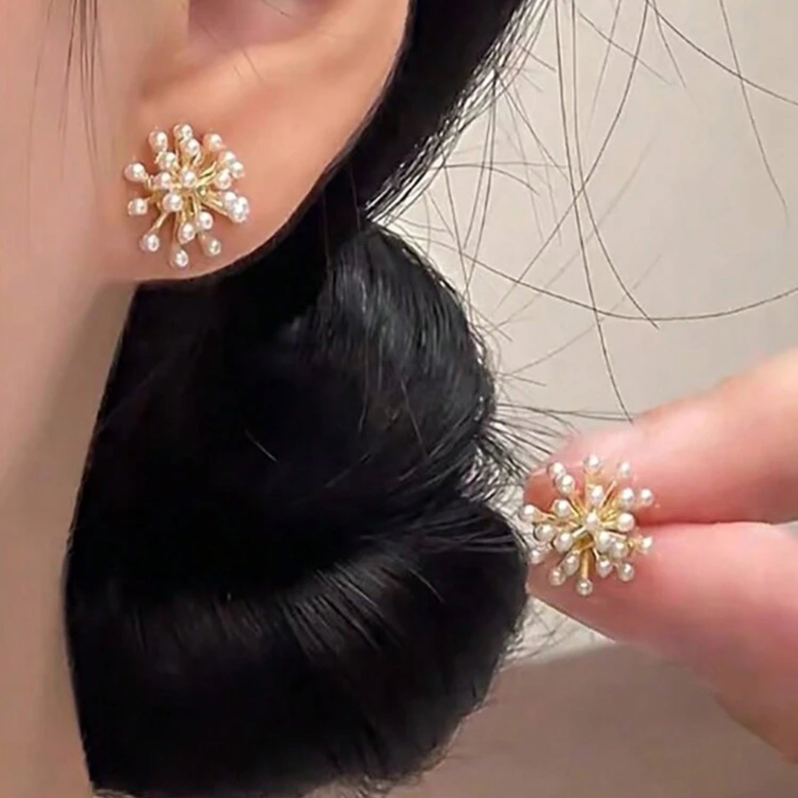 Close-up of a person wearing pearl earrings with a hand holding another pair.