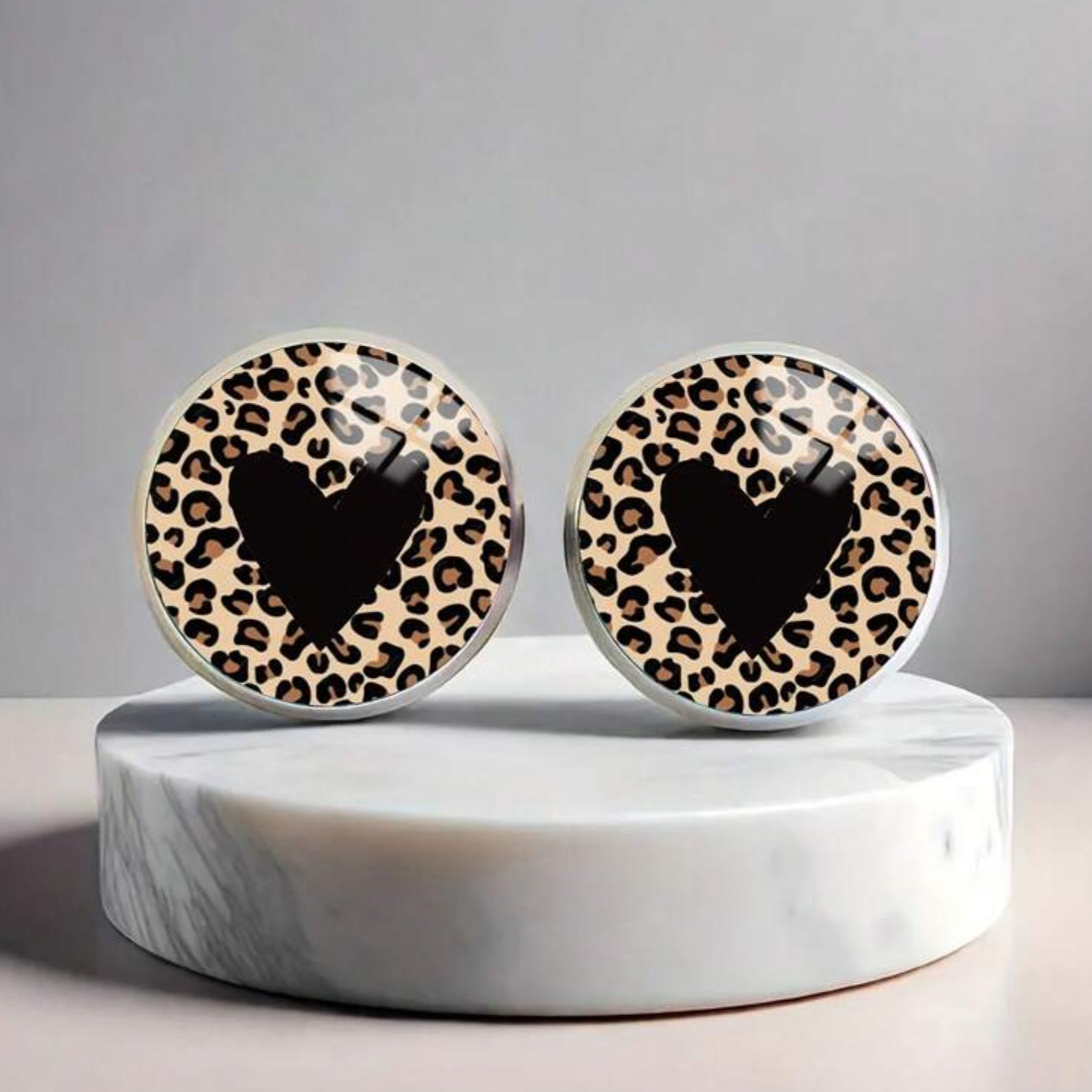 Pair of earrings with leopard print pattern on a marble stand against a gray background
