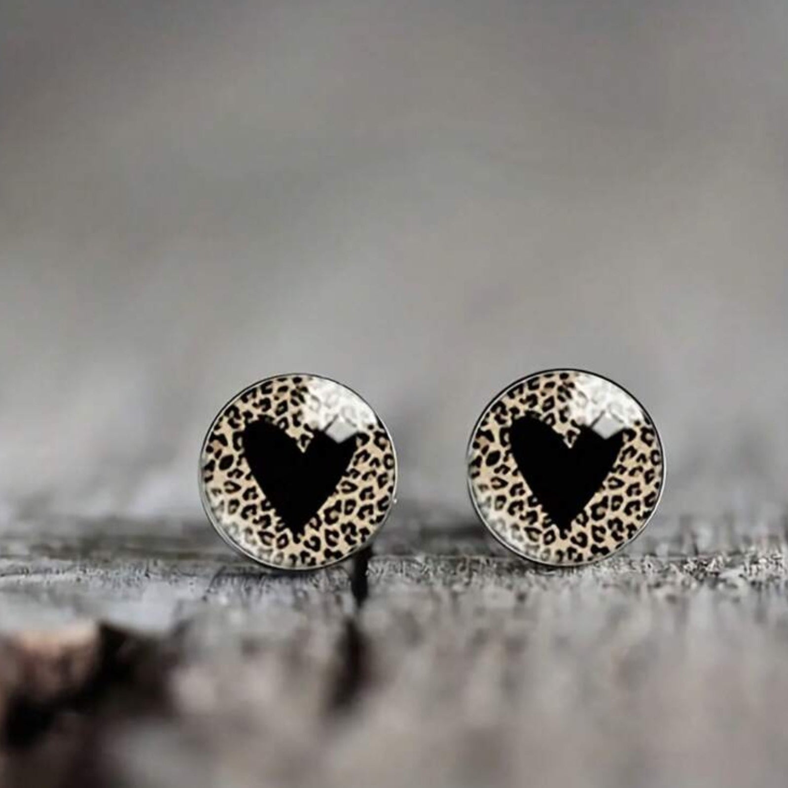 Pair of round earrings with black heart design on a textured surface